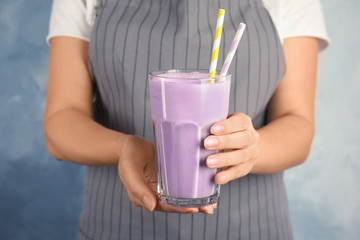 Woman with glass of delicious milk shake on color background, closeup