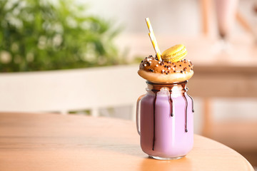 Mason jar with delicious milk shake on table against blurred background. Space for text