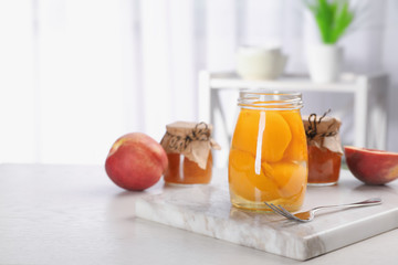 Glass jar with conserved peach halves on table. Space for text