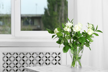 Glass vase with bouquet of beautiful roses on table in room. Space for text