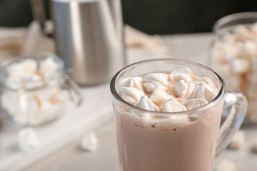 Tasty hot chocolate with milk and marshmallows in glass cup on table, closeup. Space for text