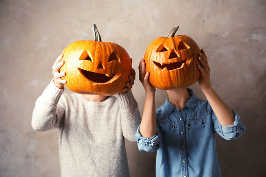 Women holding Halloween pumpkin head jack lanterns against color background