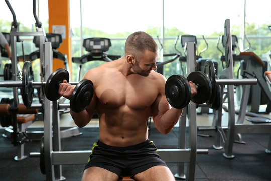 Strong young man lifting dumbbells in gym