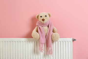 Teddy bear with knitted scarf on heating radiator near color wall