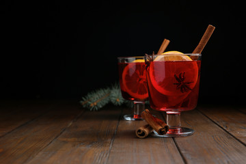 Glasses with red mulled wine on wooden table against dark background. Space for text