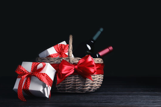 Festive basket with bottles of wine and gifts on table against dark background. Space for text