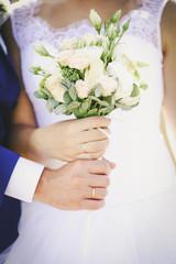 hands of the newlyweds on the wedding bouquet