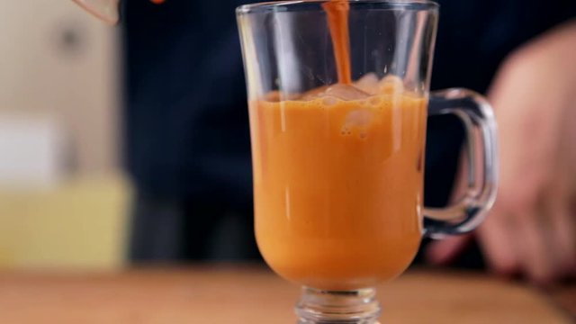 Pitcher pours Thai iced tea into a glass