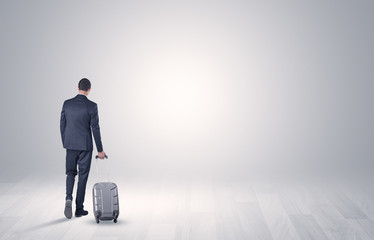 Fototapeta premium Young businessman in a white boundless space walking with back and luggage on his hand