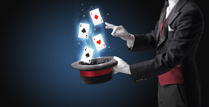 Magician with white gloves conjuring playing cards from a cylinder with magic wand