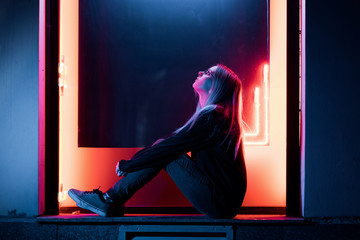 Millennial enigmatic pretty girl with unusual dyed hairstyle near glowing neon wall at night. Blue...
