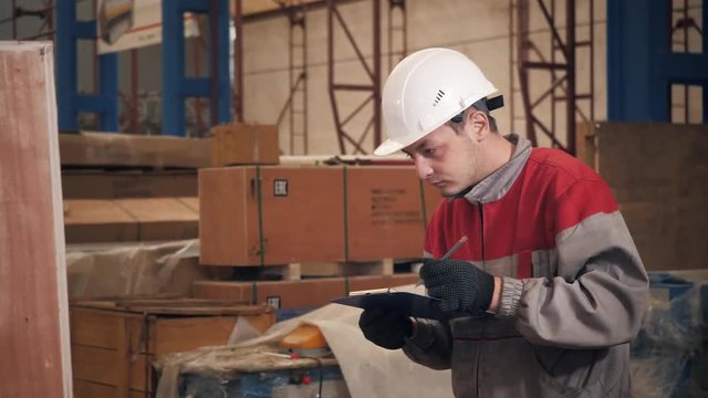 the storekeeper marks the arrival on the tablet. man driving a forklift through a warehouse in a factory. driver in uniform and protective helmet. the concept of logistics and storage