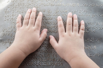 The blind kid's hand and fingers touching the Braille letters on the metal plate to understand an...
