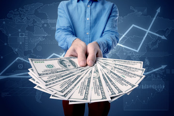 Young businessman holding large amount of bills with blue charts in the background
