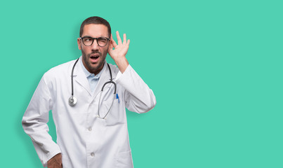 Concentrated young doctor with a gesture of trying to listen with his hand