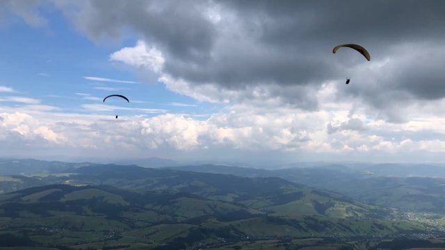 Two paragliders are flying in the sky above the mountains against the backdrop of amazing clouds.