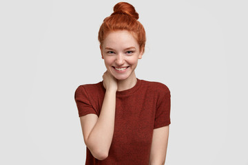 Positive shy ginger girlfriend has tender smile, keeps hand on neck, being in high spirit, rejoices...