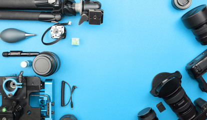 Digital camera with lenses and equipment of the professional photographer on blue paper background.