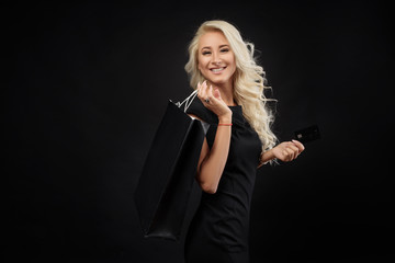 Elegant blonde woman wears  black dress holding black shopping bags and credit card,  black friday concept