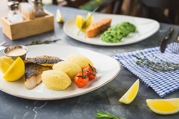 Fish dishes with millet porridge, tomato, lemon slice and shrimp sauce on table in restaurant