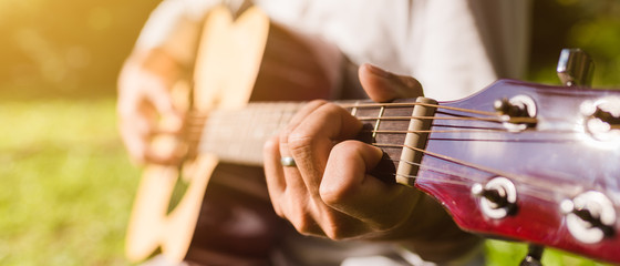 Man fingers playing guitar outdoor in summer park.