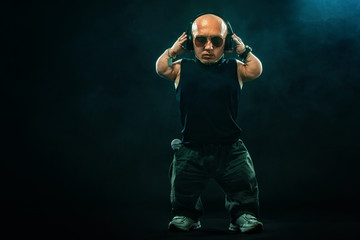 Portrait of stylish midget MC in with headphones and sunglasses posing with microphone.