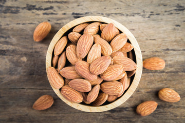 Almonds in brown bowl on textured wooden background.