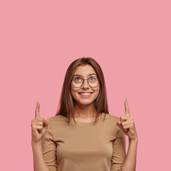 Photo of smiling Caucasian young woman with appealing appearance, toothy gentle smile, wears round...