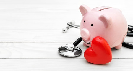 Piggy bank with stethoscope and red heart on white wooden table. Space for text. - 226168403