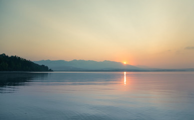 A beautiful, calm morning landscape of lake and mountains in the distance. Colorful summer scenery with mountain lake in dawn. Tatra mountains in Slovakia, Europe.