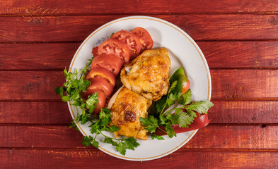 Fried chicken with vegetables on a round plate on a red wooden table.