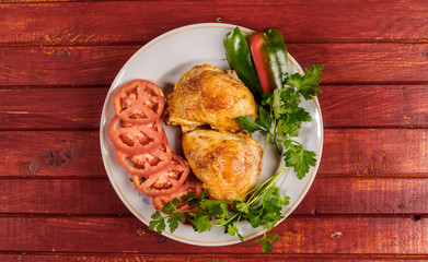Fried chicken with vegetables on a round plate on a red wooden table.
