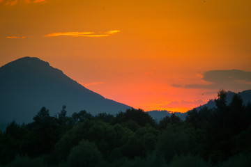 Fototapeta na wymiar A beautiful, colorful sunset landscape with lake, mountain and forest. Natural evening scenery over the mountain lake in summer. Tatra mountains in Slovakia, Europe.