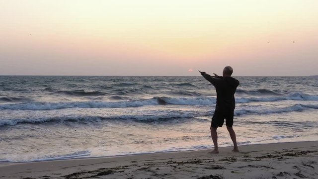 Sportive man practicing wushu on seashore at sunrise