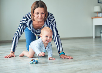 Cute baby and young mother crawling at home