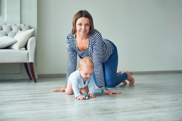 Cute baby and young mother crawling at home