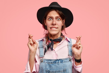 Puzzled young European gardener bites lower lip, keeps fingers crossed, waits for important...