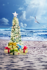 Decorated Christmas tree on sandy beach over sea with suny and cloudy sky