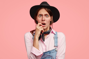 Photo of stupefied woman looks with bewildered expression, keeps finger near opened mouth, keeps...