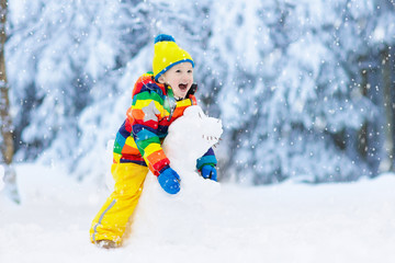 Child making snowman. Kids play in snow in winter