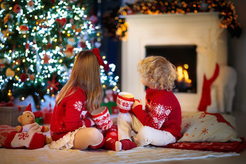 Fototapeta na wymiar Kids at Christmas tree. Children drink hot cocoa.