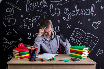 Puzzled youngster sitting at the desk with a head leaned on the hand with pointing finger under the...