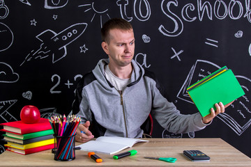 Contempt youngster sitting at the desk with a pile of books in the hand, surrounded with school...