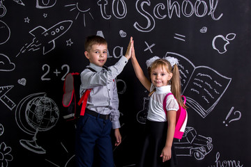 Boy and girl. School mates standing before the chalkboard as a background with a backpack on their backs claping their hands looking straight to the camera