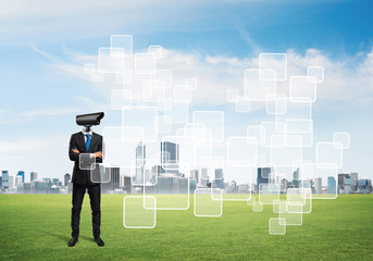 Camera headed man standing on green grass against modern cityscape