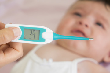 Baby sick with measuring electric thermometer. Child fever ill. Kid catch cold with temperature. Sick child in bed with fever measuring temperature with medical thermometer.