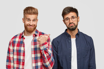 Look at this guy! Ginger bearded young man points with thumb at his fellow who has hesitant...