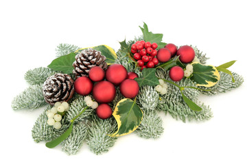 Christmas table decoration with red bauble decorations, holly berries, snow covered spruce pine, ivy, pine cones and mistletoe isolated on white background.