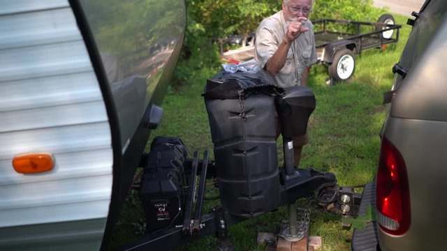 Elderly man puts the window up on his pickup truck so the poodle won&sbquo;&Auml;&ocirc;t jump out and then goes to hookup the RV to the truck.