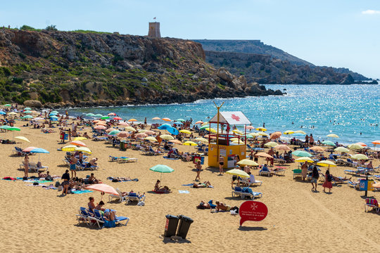 Sunbathers on the sandy beach at Golden Bay overlooked by a cliff top watchtower.- Mellieha, Malta.
